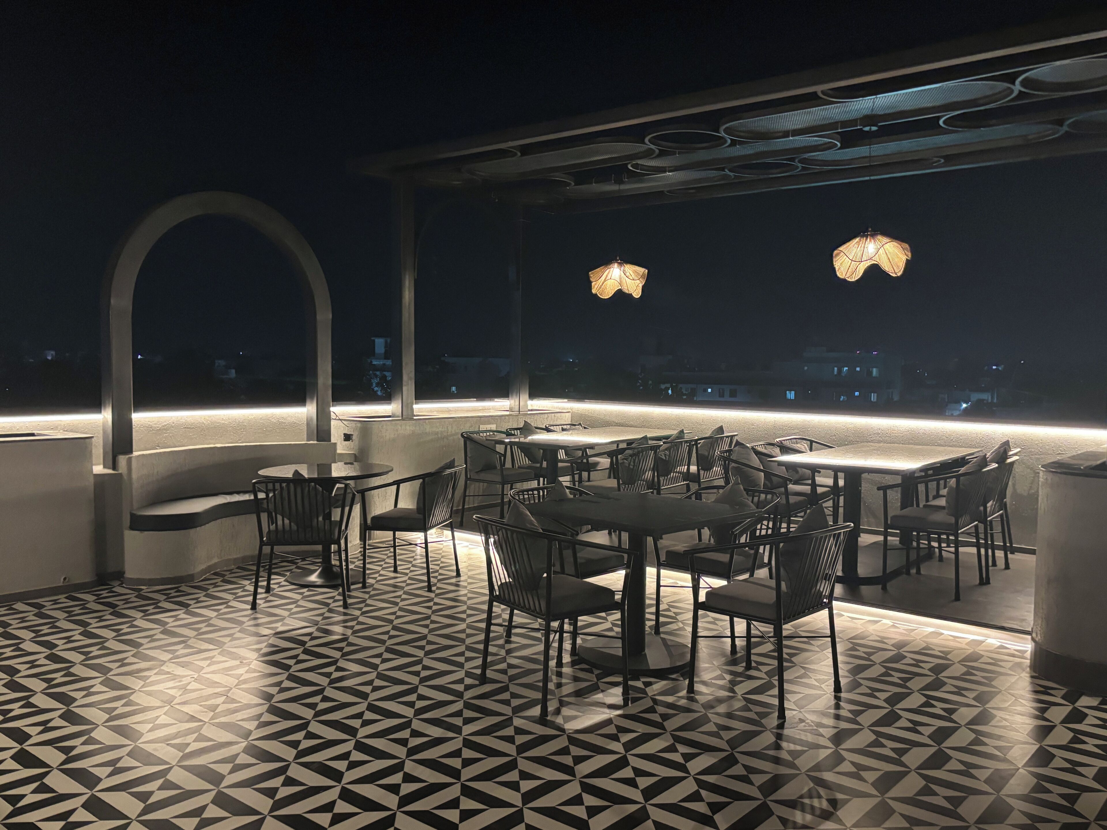 Un bar situé sur le toit, avec des tables et des chaises, un sol à motifs et des luminaires suspendus.