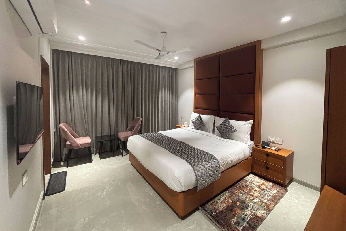 A modern bedroom with a large bed, a ceiling fan, a nightstand, and a TV.