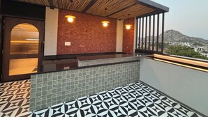 Un balcón moderno al aire libre con piso estampado, pared de ladrillo y vista a un paisaje urbano y montañas al fondo.