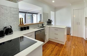A modern kitchen with a built-in stove, a sink, and a dishwasher. There are wooden cabinets and a white countertop.