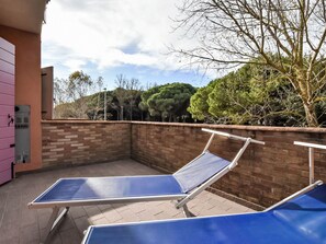 A rooftop terrace with two blue sun loungers, a brick wall, and a view of trees and a building in the background. - Solmare by Interhome (Rosolina Mare)