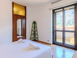 A bedroom with a bed, a green shelf, a wooden door with a mirror, and a sliding glass door leading to an outdoor area. - Como Lake Blu & Green by Interhome (Dervio)