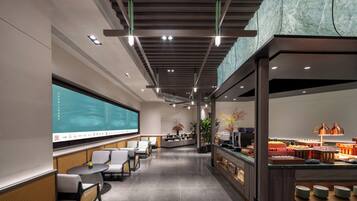 Un moderno vestíbulo de hotel con una gran pantalla digital, zona de estar y un mostrador de buffet.