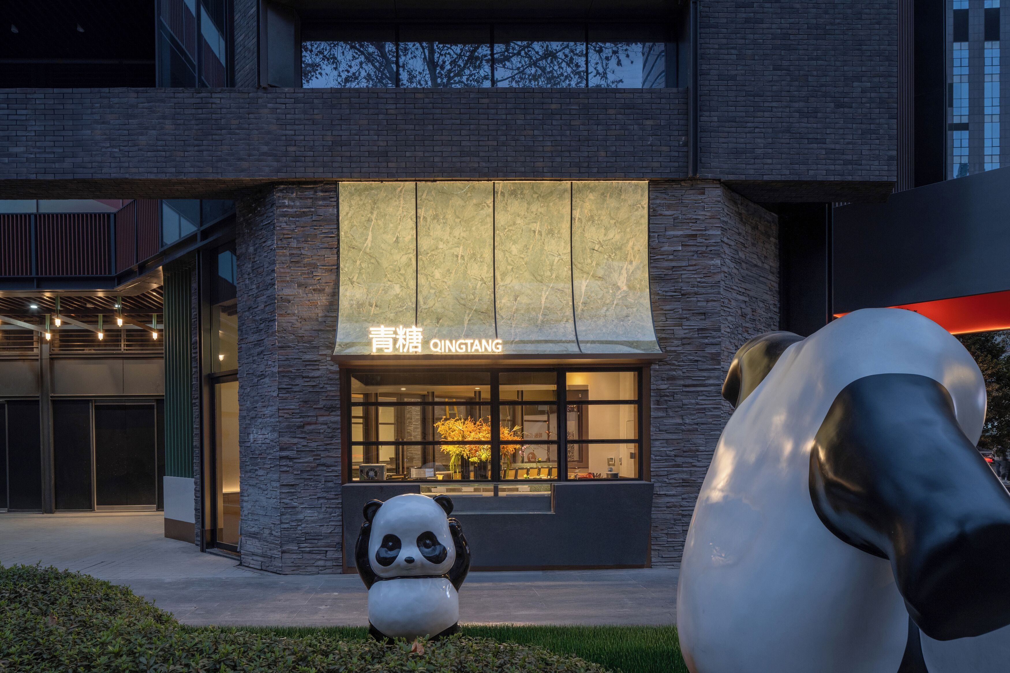 A modern building with a stone facade and a large panda sculpture in front.