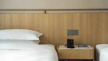 Habitación de hotel con dos camas, cabecera de madera, mesita de noche con un teléfono y un libro, y un enchufe.