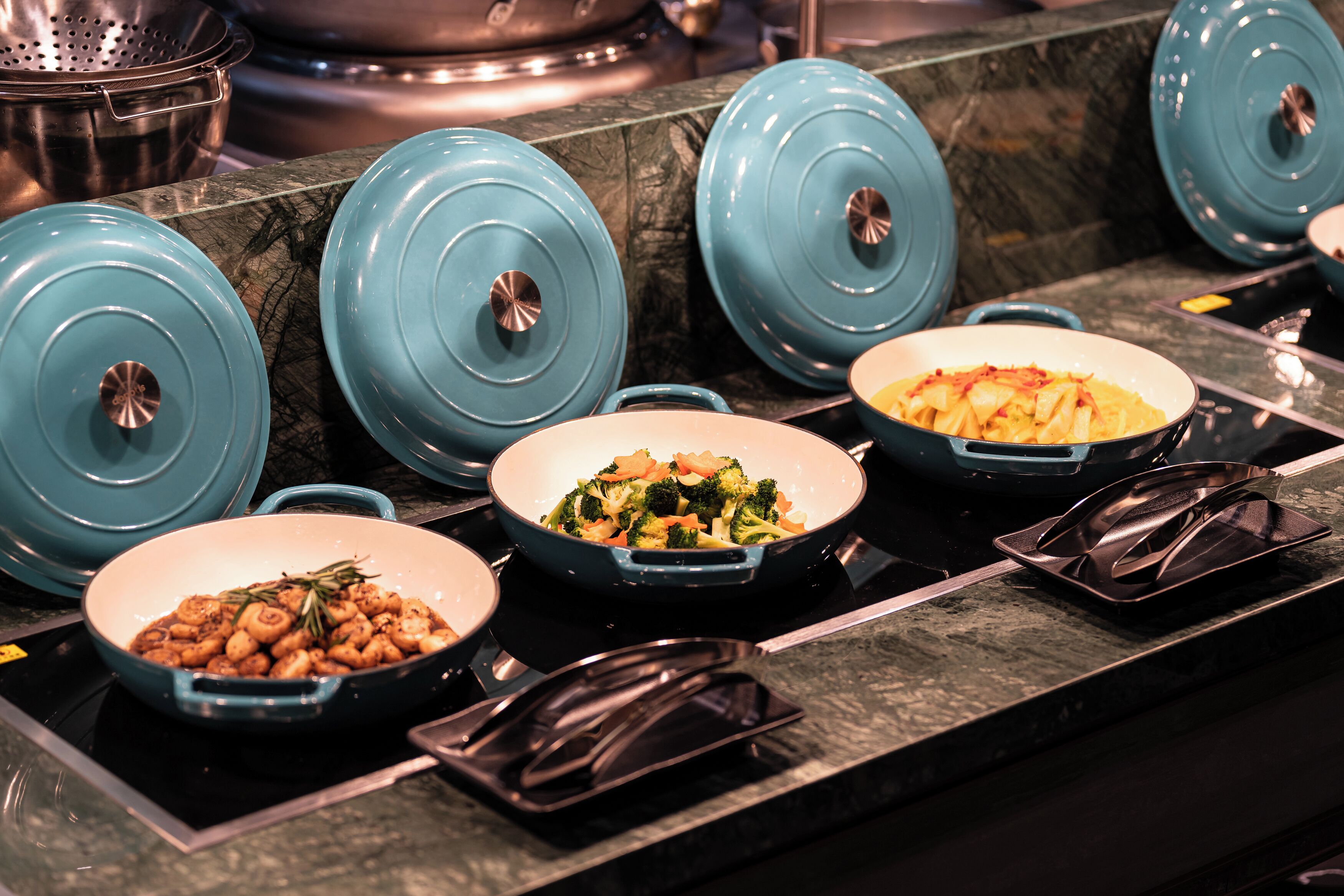 A kitchen counter with several blue covered pots and pans, a black tray, and a dish with vegetables.
