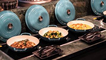 A kitchen counter with several blue covered pots and pans, a black tray, and a dish with vegetables.