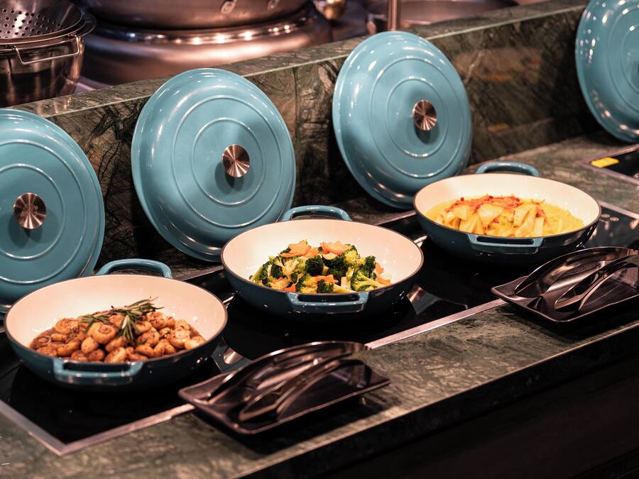 A kitchen counter with several blue covered pots and pans, a black tray, and a dish with vegetables.