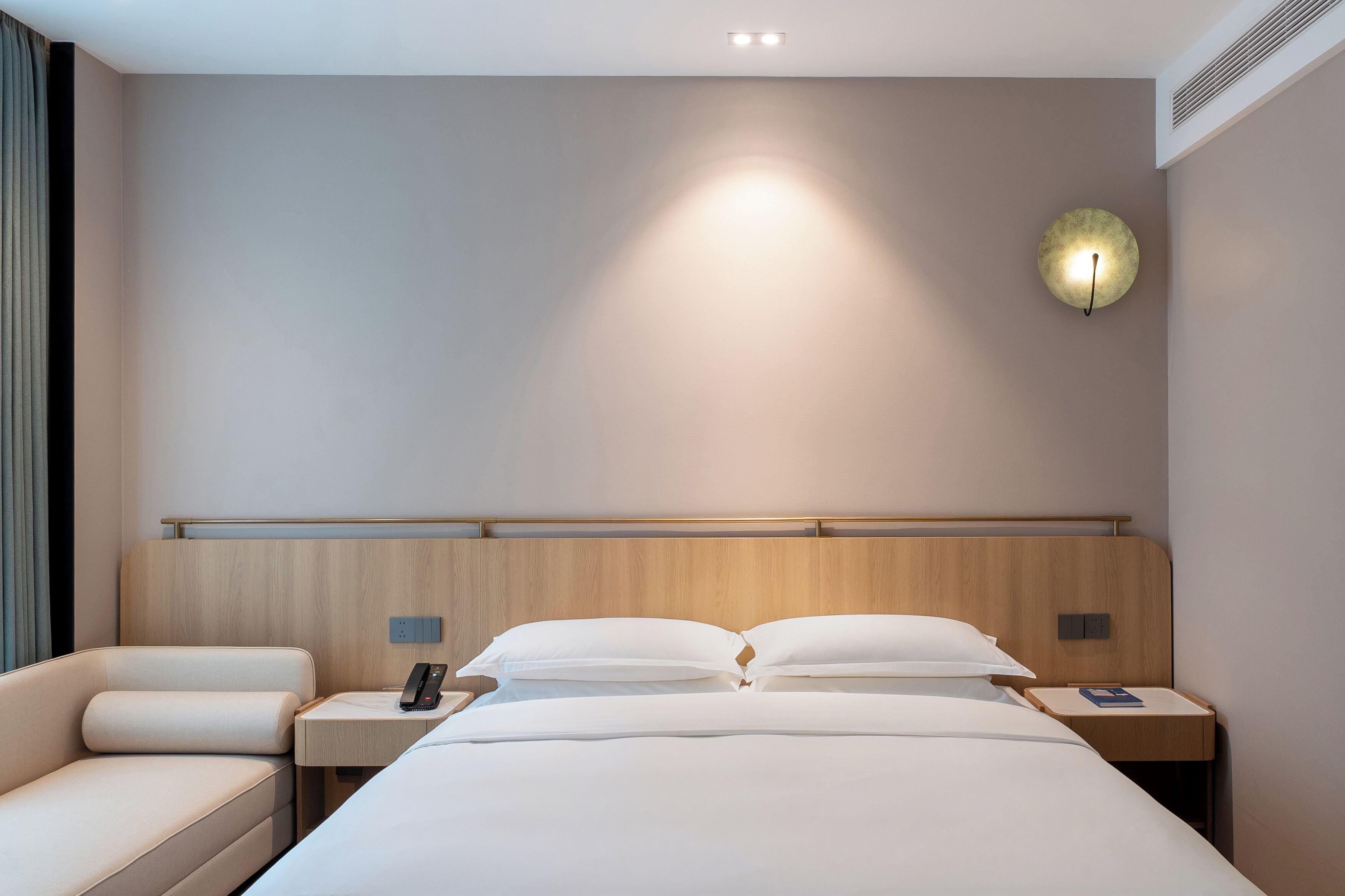 A hotel room with a bed, bedside tables, a bedside lamp, and a wall-mounted light fixture.