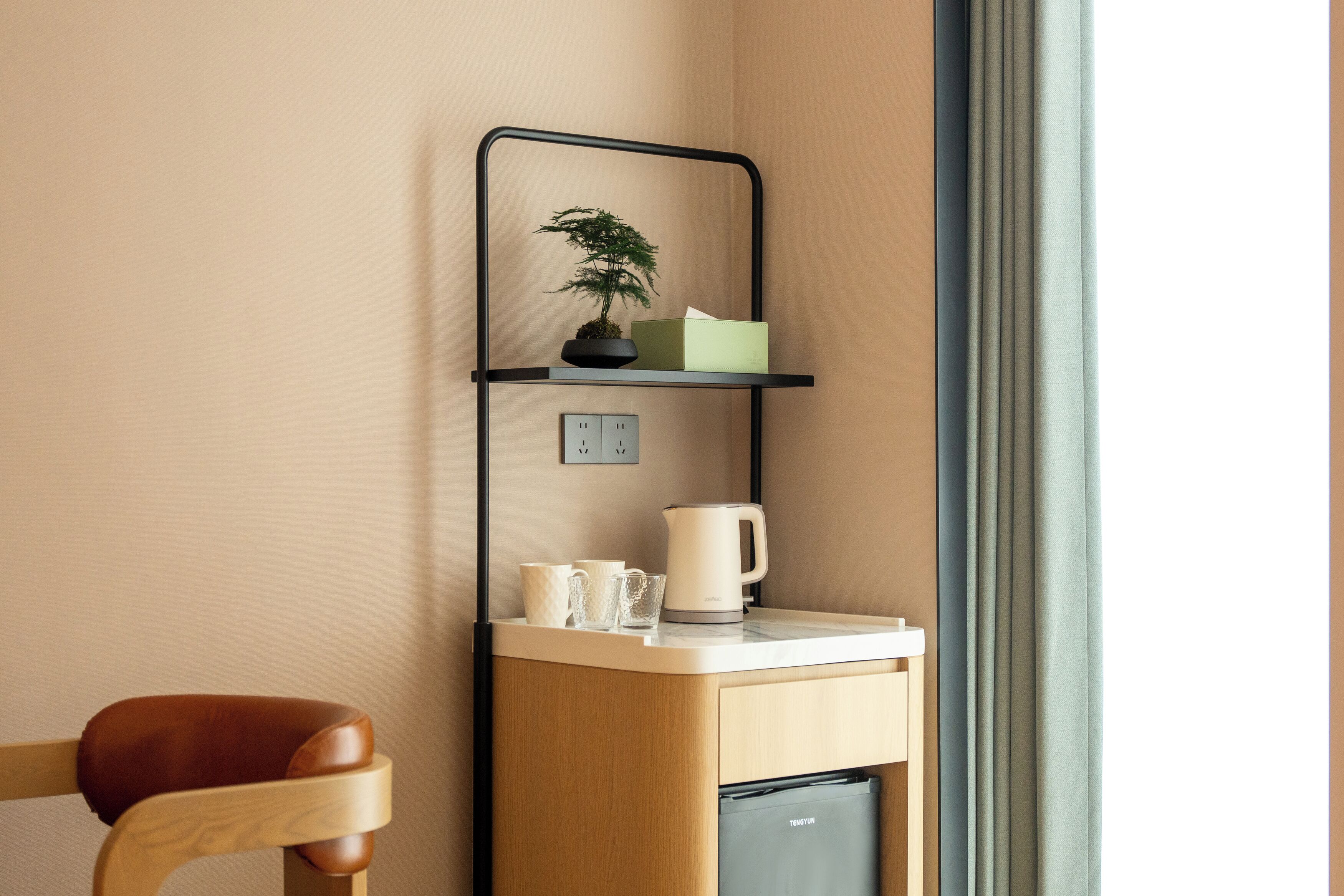 Una kitchenette con una cafetera, tazas y una planta en maceta sobre una repisa.