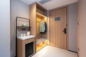 A modern hotel room with a built-in wardrobe, a small seating area, and a countertop with a coffee maker and glasses.