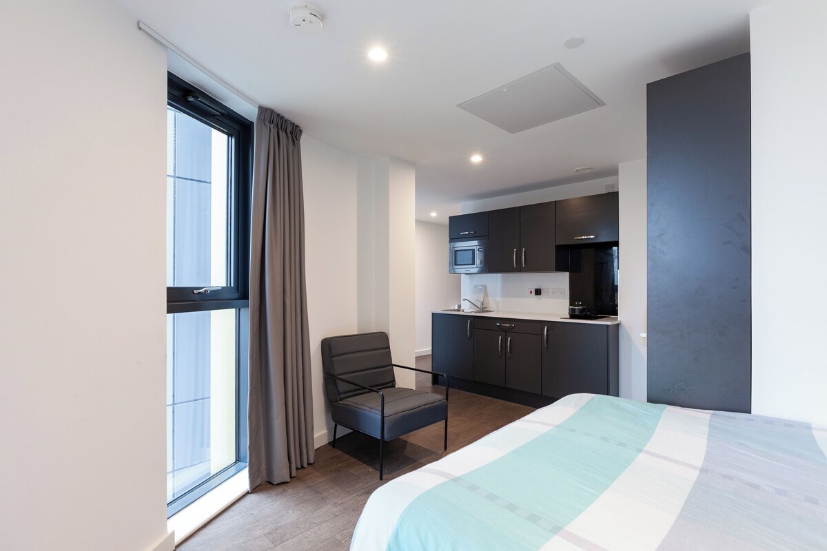 Ein modernes Hotelzimmer mit einem großen Bett, einer Sitzecke, einer Küchenzeile und einem Fenster mit Vorhängen.