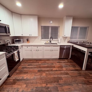 Una cocina moderna con armarios blancos, horno empotrado, microondas, lavamanos y piso de madera.