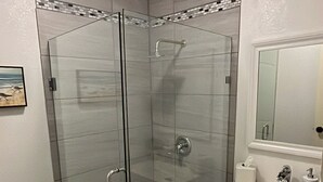 A bathroom with a glass-enclosed shower, a sink with a mirror, and a toilet. - Your coastal escape starts here! (Playas de Rosarito, BC Mexico)