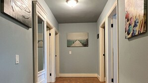 A hallway with a tiled floor, a ceiling light, and artwork on the walls. - Your coastal escape starts here! (Playas de Rosarito, BC Mexico)