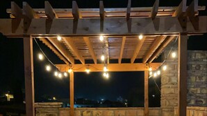 A covered outdoor patio area with a wooden pergola, string lights, stone walls, and potted plants. - Your coastal escape starts here! (Playas de Rosarito, BC Mexico)
