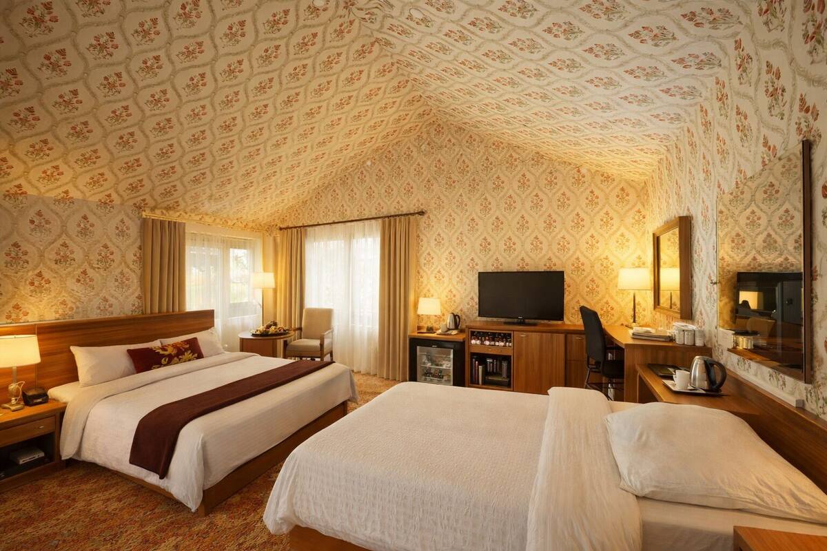 Habitación de hotel con dos camas, televisión, escritorio y espejo.