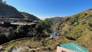 A mountainous landscape with a clear sky. There are buildings and a bridge in the valley. - Yao Adventure Base Camp Bhatta Falls (Mussoorie)