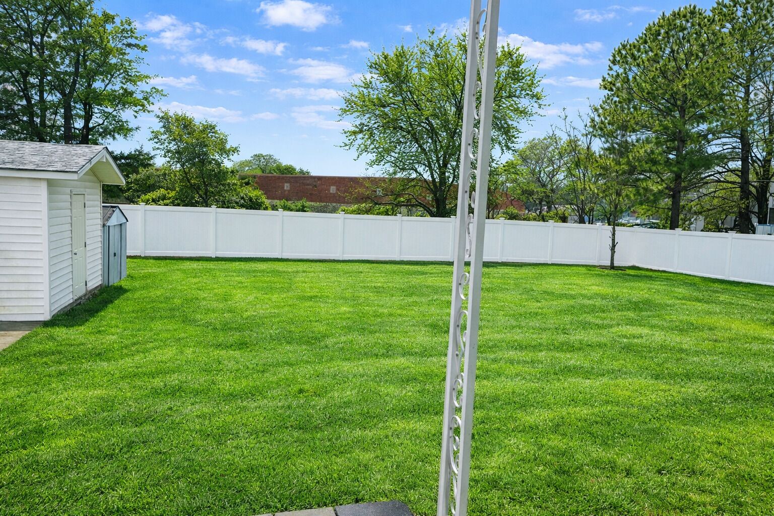 A backyard with a white fence, a shed, and a well-maintained lawn.