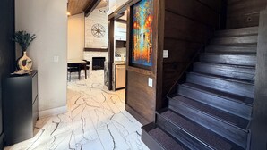 Un intérieur moderne avec un sol en marbre, un escalier en bois et un coin repas agrémenté d’une cheminée.