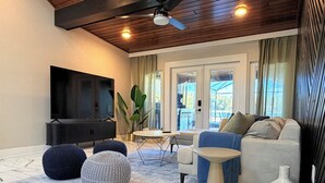 Un salon moderne comprenant un téléviseur à écran plat, un canapé, des poufs ronds, une table basse et un vase décoratif.