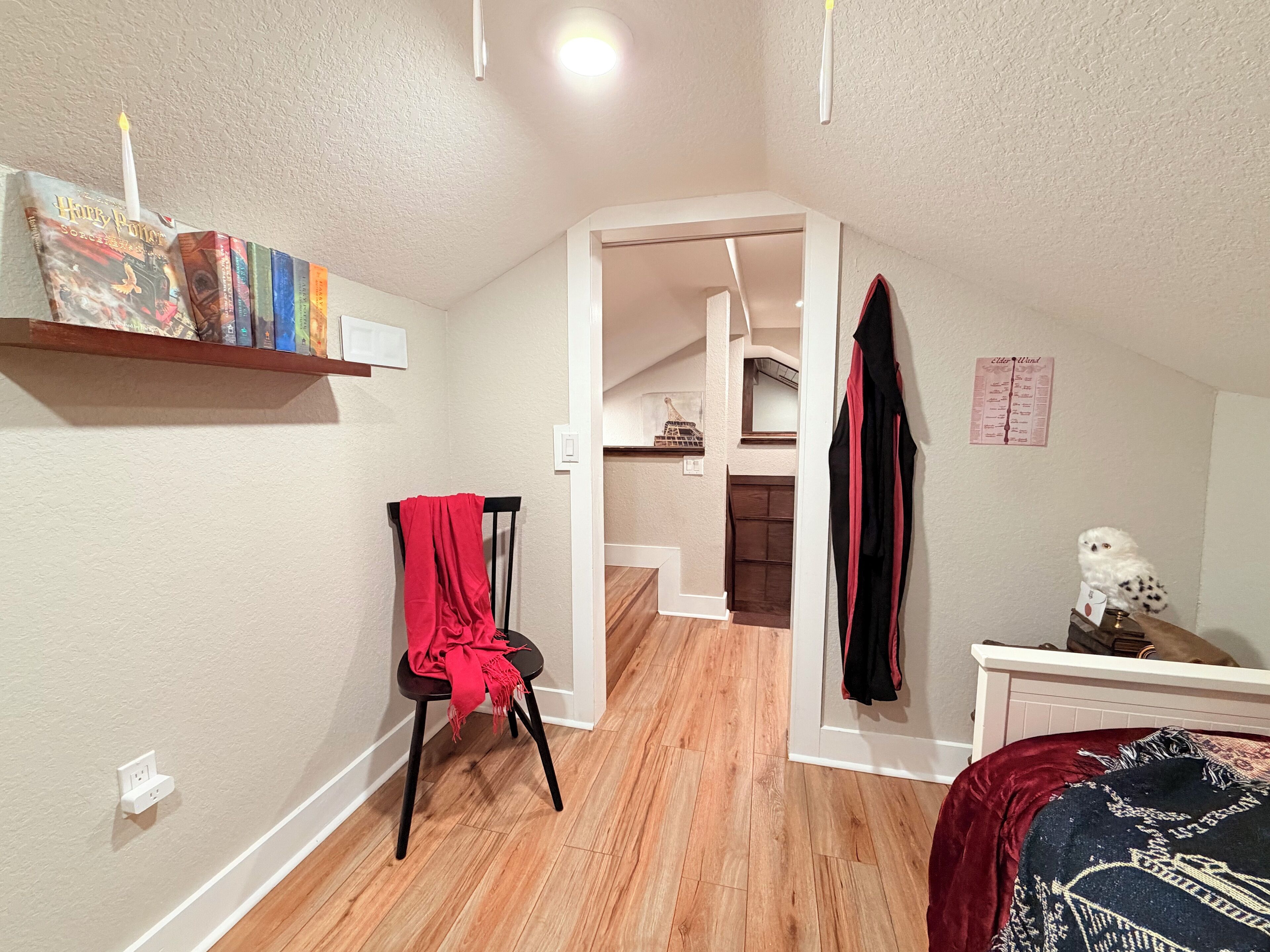 Un dormitorio con piso de madera, una silla roja, una cama blanca y una estantería con libros.