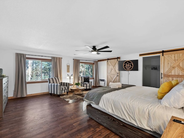 Une chambre spacieuse avec un grand lit, un ventilateur de plafond, une télévision et une armoire en bois.