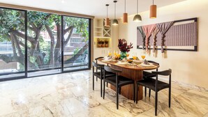A dining area with a large window, a wooden dining table, black chairs, and pendant lights. - Hotel Boutique Kooben  (Merida)