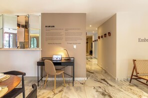 A modern hotel room with a desk, chair, and a laptop. There is a wall with text and a hallway with a bench. - Hotel Boutique Kooben  (Merida)