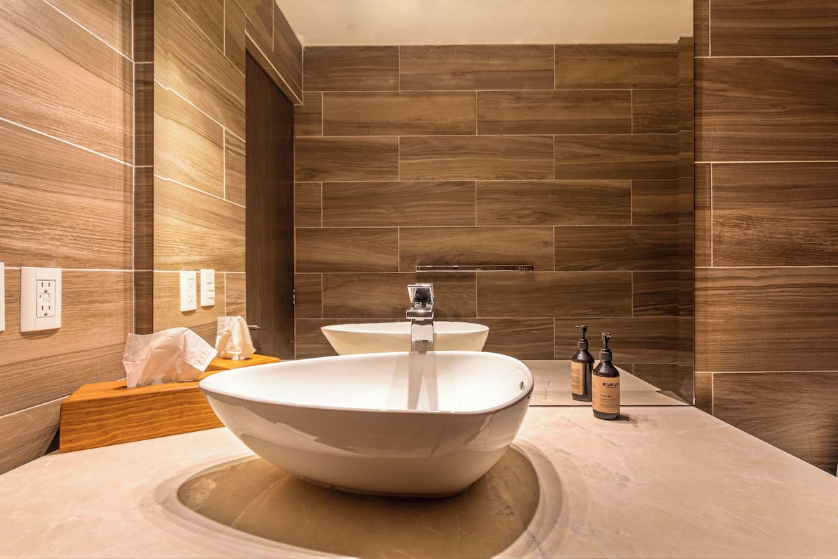 A modern bathroom with a large vessel sink, two faucets, and a wooden vanity.