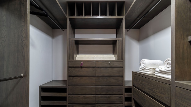 A walk-in closet with multiple drawers and shelves, a wooden floor, and a door on the left. - Hotel Boutique Kooben  (Merida)