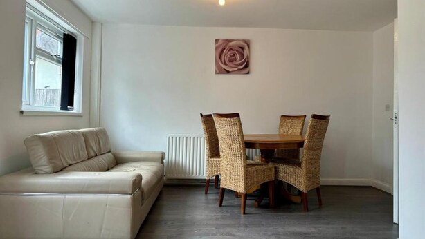 A room with a beige sofa, a dining table with wicker chairs, a radiator, and a ceiling light. - Family Ensuite in Dudley (Dudley)
