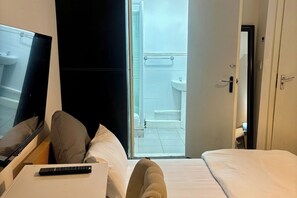 A hotel room with a bed, a TV, a remote control, and an open door leading to a bathroom. - Family Ensuite in Dudley (Dudley)