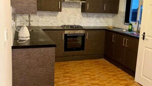 A kitchen with dark cabinets, a built-in oven, and a tiled floor. - Family Ensuite in Dudley (Dudley)