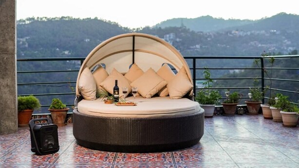 Ein runder Sitzbereich im Freien aus Weidengeflecht mit Kissen, einer Flasche und Gläsern auf einer gefliesten Terrasse mit Topfpflanzen und einem schönen Bergblick.