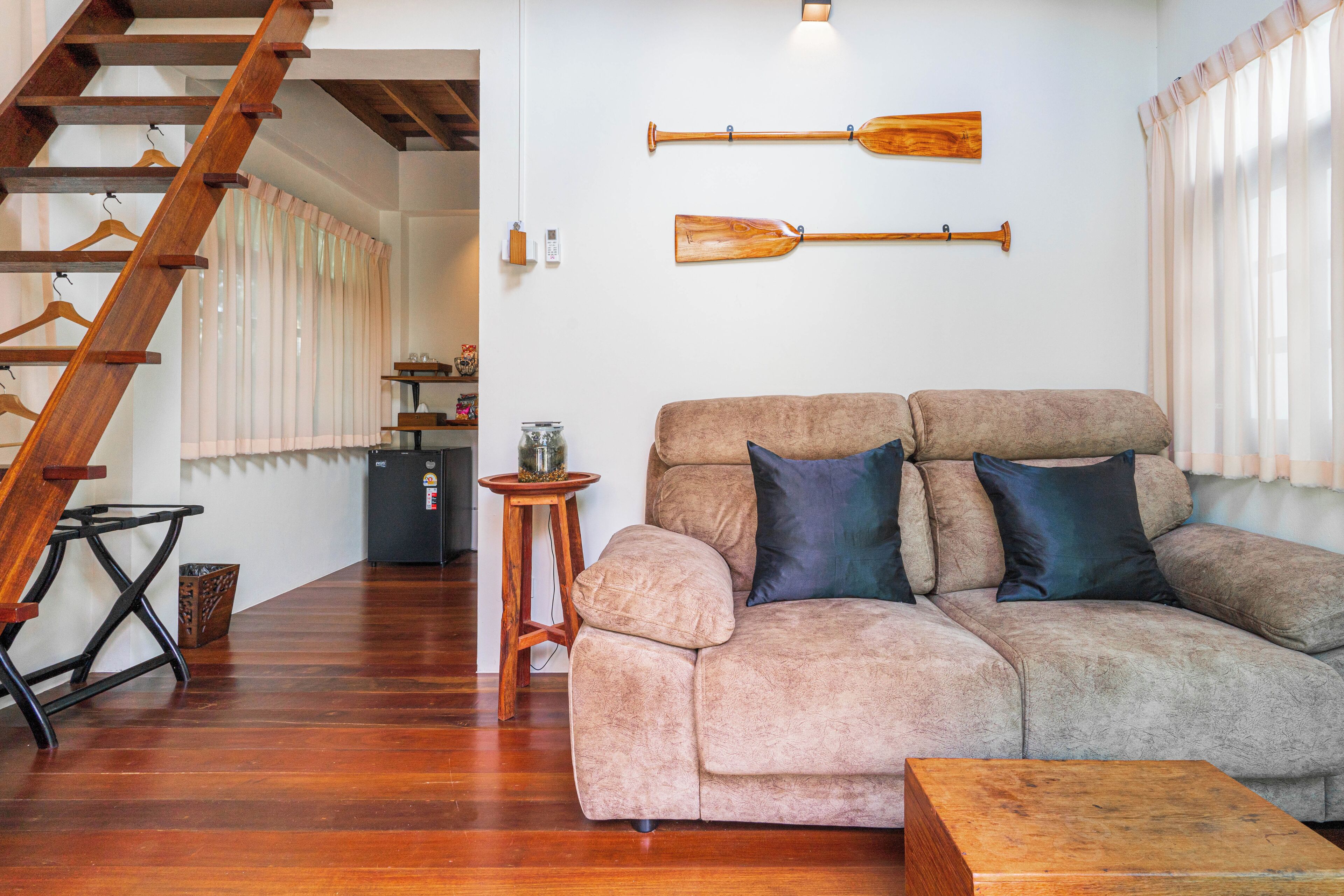 A living room with a wooden staircase, a sofa, and two wooden paddles on the wall.