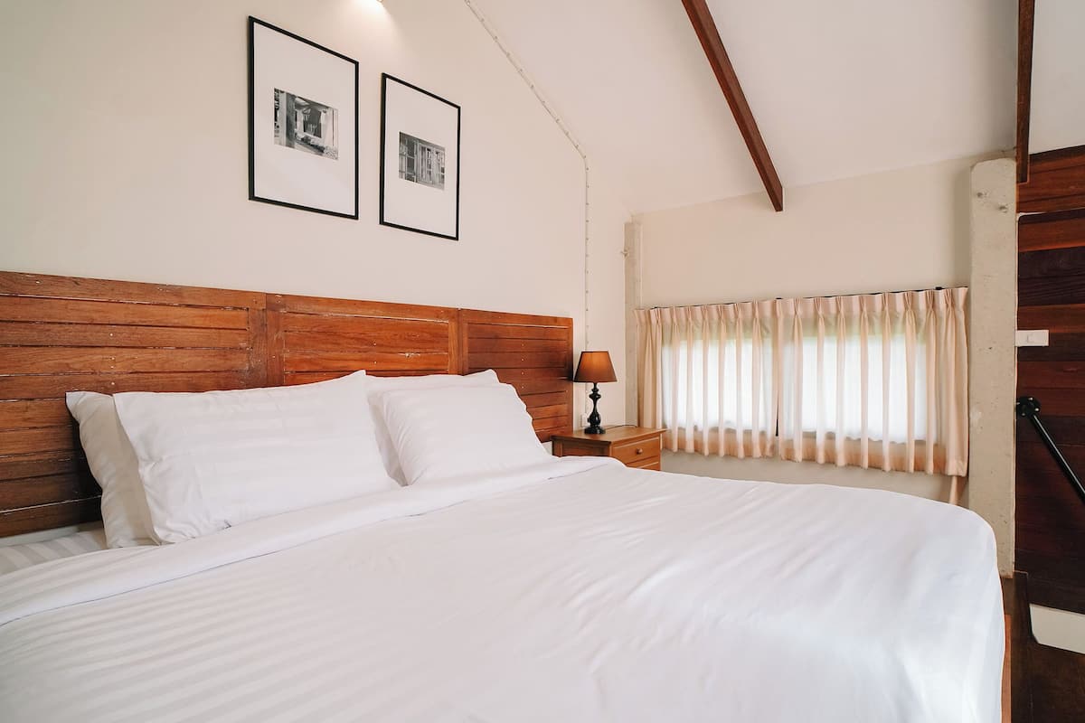 A neatly made bed with white linens, a wooden headboard, and two framed pictures on the wall.
