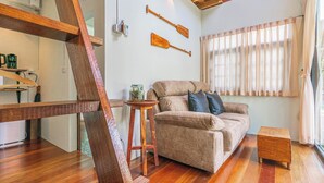 A cozy living room with a wooden ladder, a sofa, and two wooden paddles on the wall. - Baanrongmai Canal Front Homestay (Phra Pradaeng)