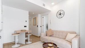 Uma sala de estar moderna com um sofá bege, uma mesa de centro redonda e um relógio de parede.