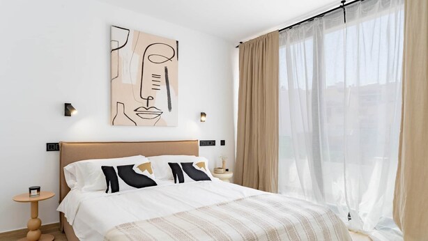 Quarto moderno com uma cama grande, uma obra de arte na parede, mesas de cabeceira e cortinas leves.