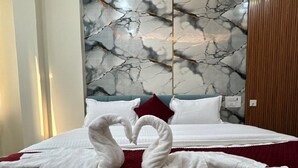 Une chambre d’hôtel avec un lit, deux serviettes en forme de cygne, un mur décoré d’un motif imitant le marbre et un panneau en bois sur le côté droit.