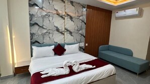 Une chambre d’hôtel moderne avec une tête de lit à motifs de marbre, un lit avec du linge de lit blanc, un canapé bleu et un ventilateur de plafond.