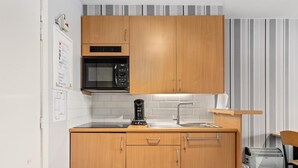 Cocina compacta con armarios de madera, microondas, cafetera y lavamanos.