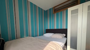 Un dormitorio con cama, papel tapiz a rayas, un armario y una ventana.