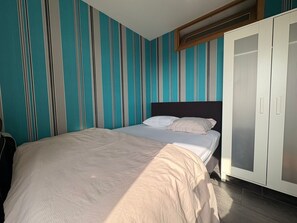 A bedroom with a bed, striped wallpaper, a wardrobe, and a window. - Sunny apartment with sea-views (Blankenberge)