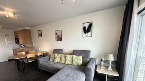 Una sala moderna con un sofá gris, una mesa de comedor y una cocina al fondo.