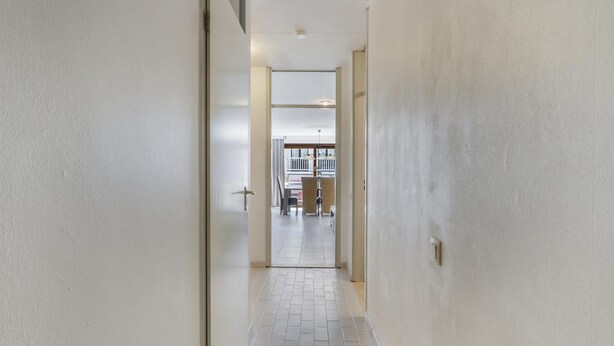 A narrow hallway with white walls and a tiled floor leading to a room with a balcony. - Pleasant apartment near the beach (Blankenberge)