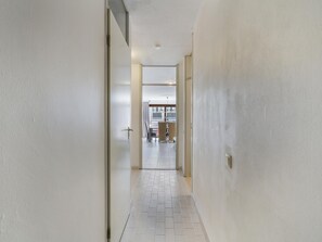 A narrow hallway with white walls and a tiled floor leading to a room with a balcony. - Pleasant apartment near the beach (Blankenberge)