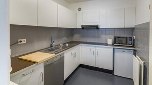 A compact kitchen with white cabinets, a dishwasher, a microwave, and a sink. - Pleasant apartment near the beach (Blankenberge)