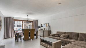 A modern living room with a sofa, coffee table, and dining area. - Pleasant apartment near the beach (Blankenberge)